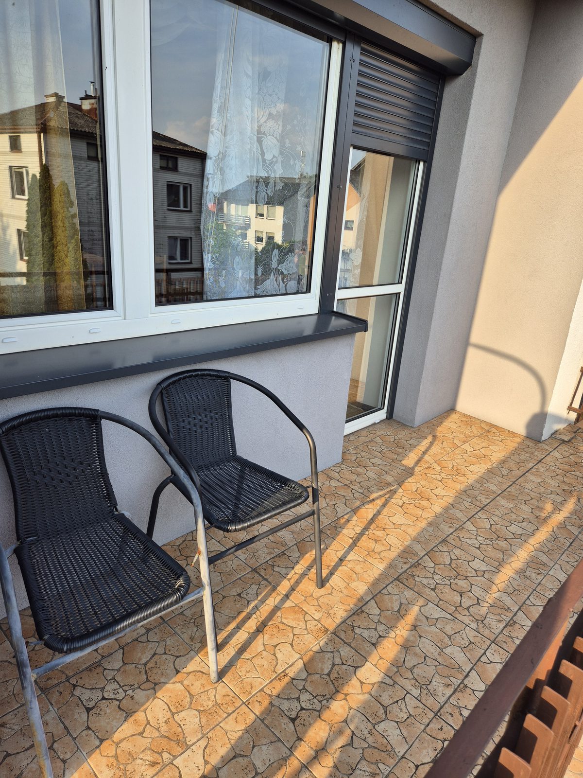 Balkon z dwoma plecionymi fotelami i widokiem na okolicę.